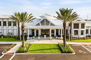 Ein modernes Hotel mit überdachter Eingangsparte, Palmen und Parkplatz.