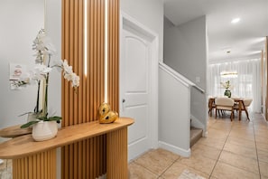 A modern interior with a wooden reception desk, white orchid flowers, and a staircase leading to a dining area. - 4 Bd / 3 Ba / Sleeps 11/ Storey Lake Resort (Kissimmee)