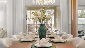 Comedor con una mesa preparada para cuatro personas, un florero verde con flores y una araña.