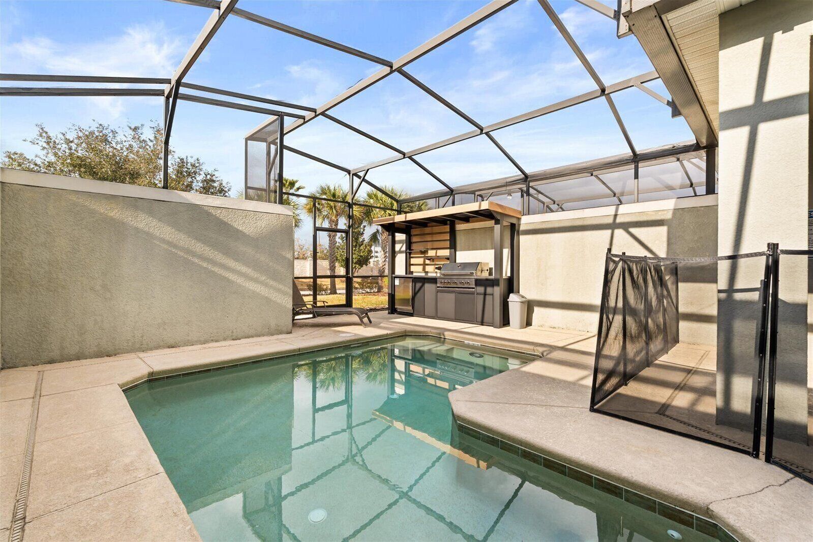 Un área de piscina con una estructura de cristal, una zona de barbacoa y una silla de descanso.