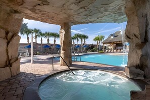 A hot tub area with a pool, stone pillars, and a covered seating area with umbrellas. - 5 Bd / 4 Ba / Sleeps 12 / Paradise Palms Resort (Kissimmee)