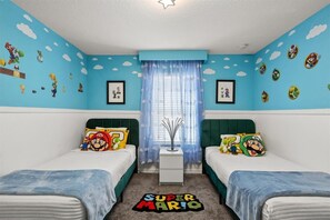 Une chambre avec deux lits, des murs bleus et une décoration sur le thème de Super Mario.
