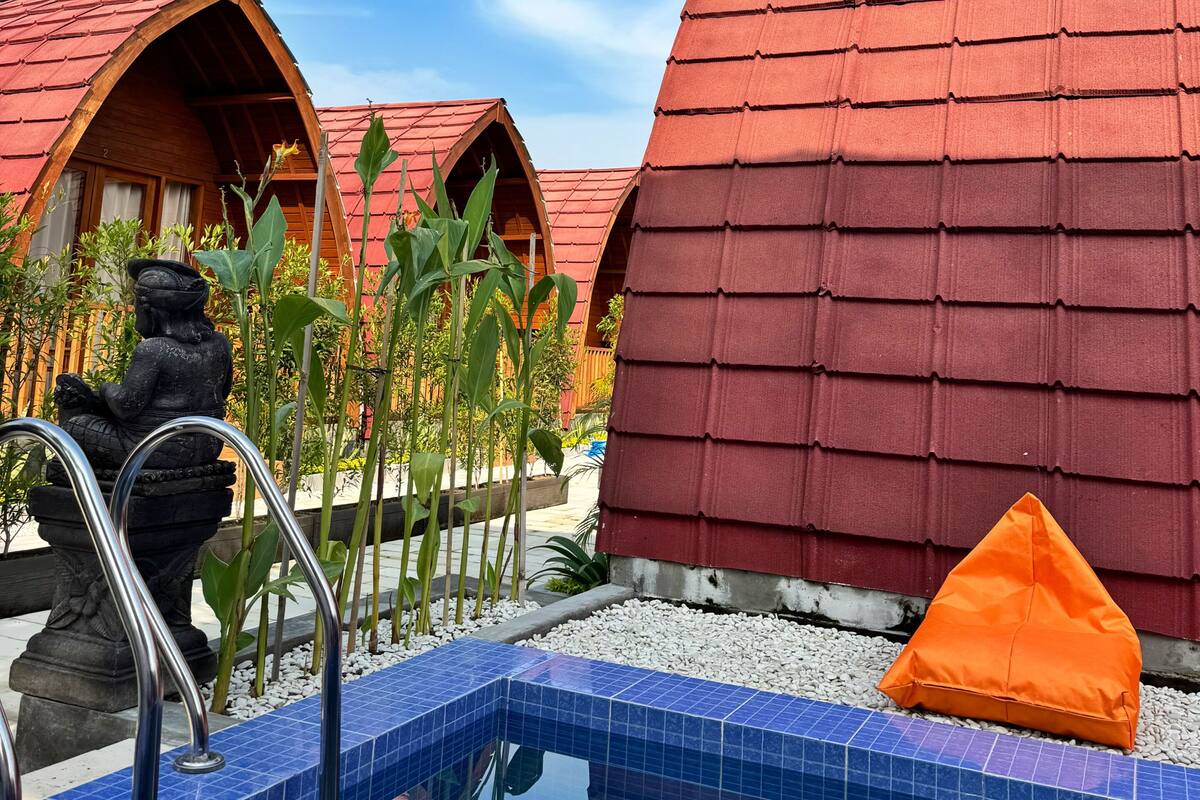 A pool area with tiled blue edges, a metal ladder, and red-roofed structures.