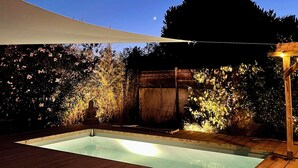 Eine Holzterrasse mit Swimmingpool, Buddha-Statue und einer Pergola.