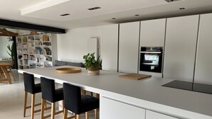 Eine moderne Küche mit weißer Arbeitsplatte, schwarzen Barhocker, Schneidebrett aus Holz und einem Blumentopf.