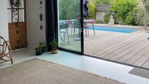 Ein modernes Wohnzimmer mit einem großen Schiebeglasfenster, das auf eine Holzterrasse und eine Außenlounge führt.
