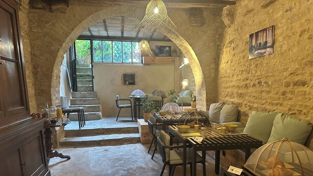 Un interior rústico con paredes de piedra, una mesa de madera preparada para el desayuno, un sofá y una escalera que lleva a un espacio al aire libre.