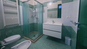 Kylpyhuone, jossa on lasiseinällä varustettu suihku, valkoinen pesuallas ja wc.