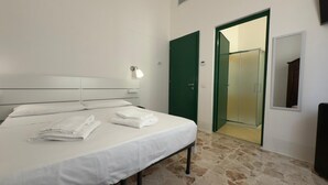 Hotellihuone, jossa on sänky, vihreä ovi, suihku ja peili.