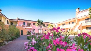 A courtyard with pink flowers, a brick pathway, and pastel-colored buildings. - Pomposa Residence (Lido di Pomposa)