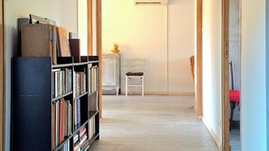 Un pasillo amplio con una estantería, un banco y una puerta que da a otra habitación.