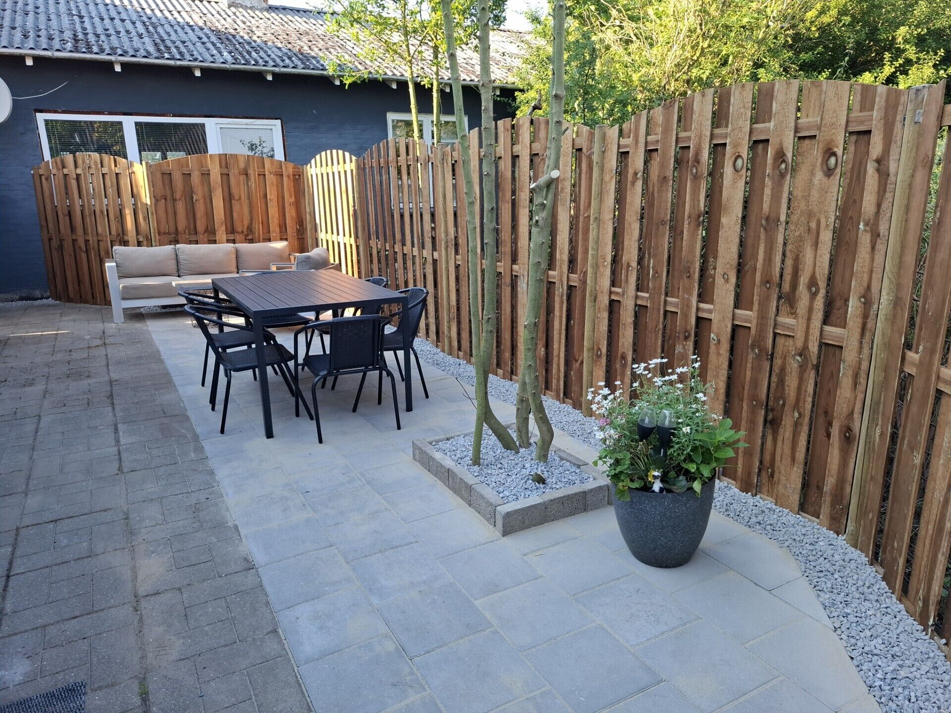 Une terrasse avec une table et des chaises, une clôture en bois et un pot de fleurs.