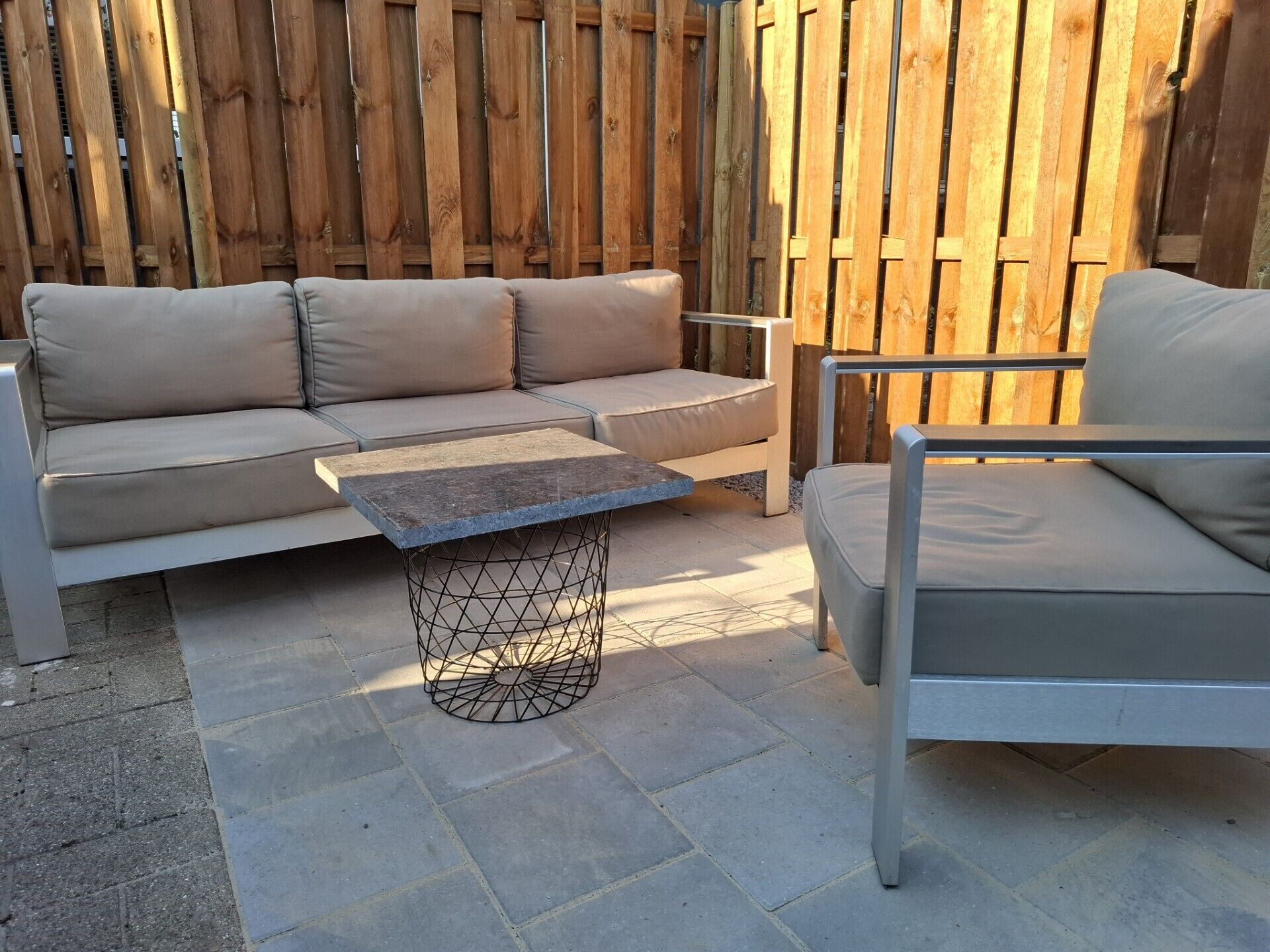 Eine Terrasse mit einer beigen Couch, einem Metall-Couchtisch und einem Metallstuhl.
