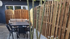 A patio area with a wooden table and chairs, a potted plant, and a wooden fence. - The Cozy Cottage – Charming Holiday Home near the North Sea (Hirtshals)