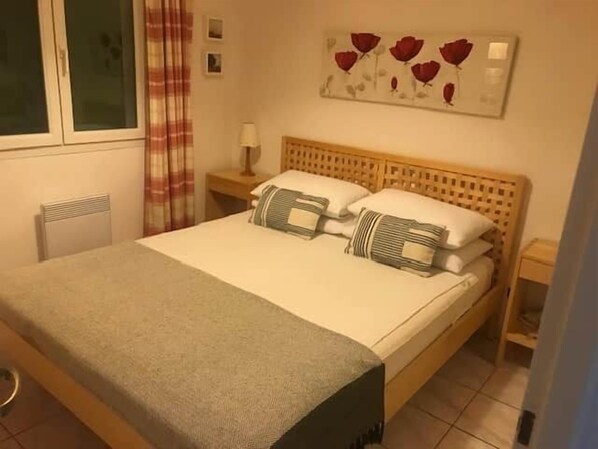 A neatly made bed with a grey blanket, a wooden headboard, and two bedside tables with lamps.