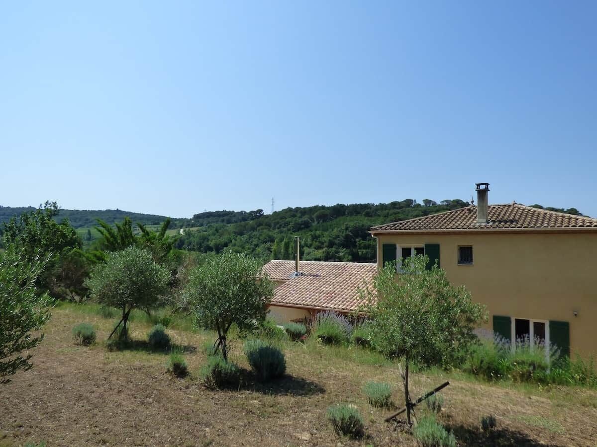 A rural house with a tiled roof, surrounded by olive trees and a clear sky.