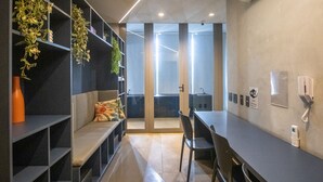 Ein moderner Arbeitsraum mit Schreibtisch, Stühlen, Pflanzenregalen, einer Couch und Blick durch eine Glastür.