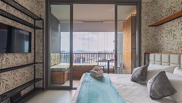 Ein modernes Hotelzimmer mit Balkon, einem Bett mit Kissen, einem an der Wand montierten Fernseher und Wandtapete mit Muster.