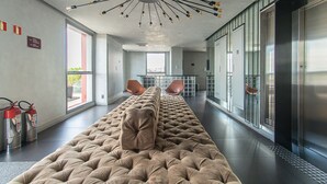 Eine moderne Hotelhalle mit einer langen, gesteppten Couch, einer außergewöhnlichen Deckenleuchte und einem Feuerlöscher an der Wand.