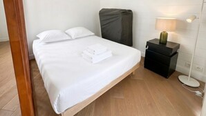 Ein ordentlich bezogenes Bett mit weißen Bettwäsche, ein Nachttisch mit Lampe und ein Gegenstand an der Wand, der mit Stoff bedeckt ist.
