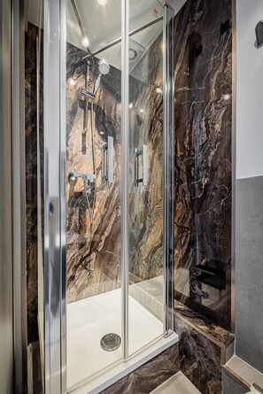 Eine bodenebene Dusche mit Glastür, Marmorwänden und einer weißen Badewanne.