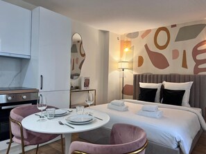 A modern hotel room with a dining area, a bed with a headboard, and a wall with abstract art. - 1D#Studio 2 pers#Bon Marché#St Germain#Paris 6 (Paris)