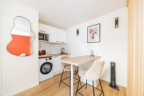 A compact kitchen with a washing machine, a wooden table, and two chairs. - 11#Studio 2 pers#Bon Marché#St Germain#Paris 6 (Paris)