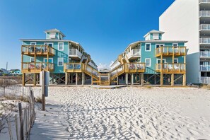 Ein Strandhotel mit zweistöckigen Gebäuden, Holzbalkonen und einem sandigen Strand im Vordergrund.