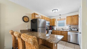A kitchen with wooden cabinets, a stainless steel refrigerator, a microwave, and a dishwasher. - ✨Beachfront Complex + Community Pool | Sleeps 4 | Sunrise Village 111✨ (Gulf Shores)