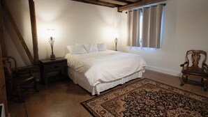 Une chambre à coucher avec un grand lit, deux tables de chevet, un tapis, une chaise et une fenêtre avec des rideaux.