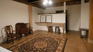 Une pièce avec un plafond en bois, un grand tapis à motifs, deux chaises en bois, une petite table et un banc.