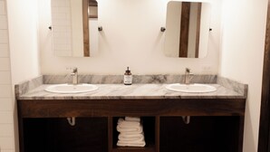Une salle de bain avec deux lavabos, chacun étant surmonté d’un miroir. Des serviettes sont suspendues sur une étagère située en dessous des lavabos.