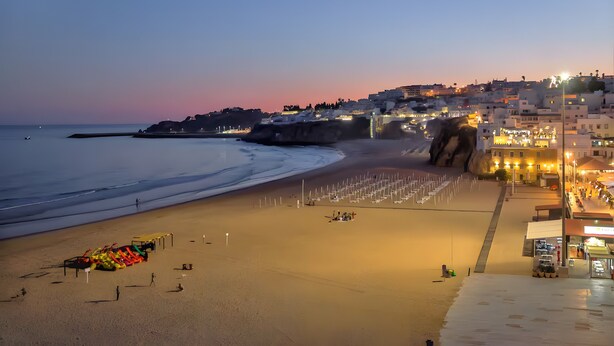 Une plage bordée d’une rangée de parasols, une tour de surveillance pour les sauveteurs et un bâtiment dont les lumières sont allumées.