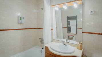 A bathroom with a bathtub, a sink, a mirror, and a toilet.