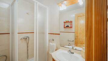 Un baño con ducha, lavamanos y espejo.