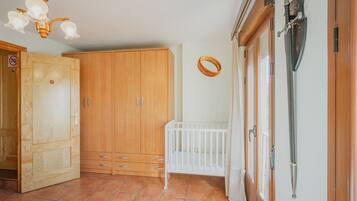A room with a wooden wardrobe, a white crib, a hanging sword, and a chandelier.