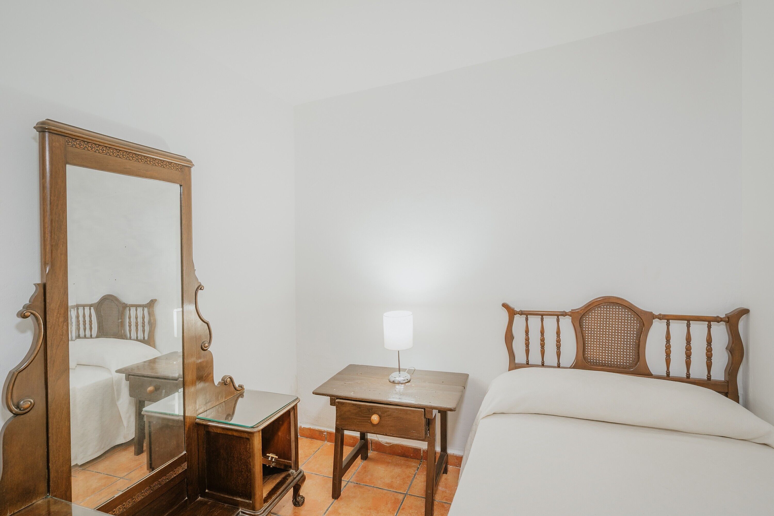 Un dormitorio con una cama de madera, una mesita de noche con lámpara, y un espejo grande.