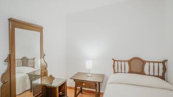 Un dormitorio con una cama de madera, una mesita de noche con lámpara, y un espejo grande.