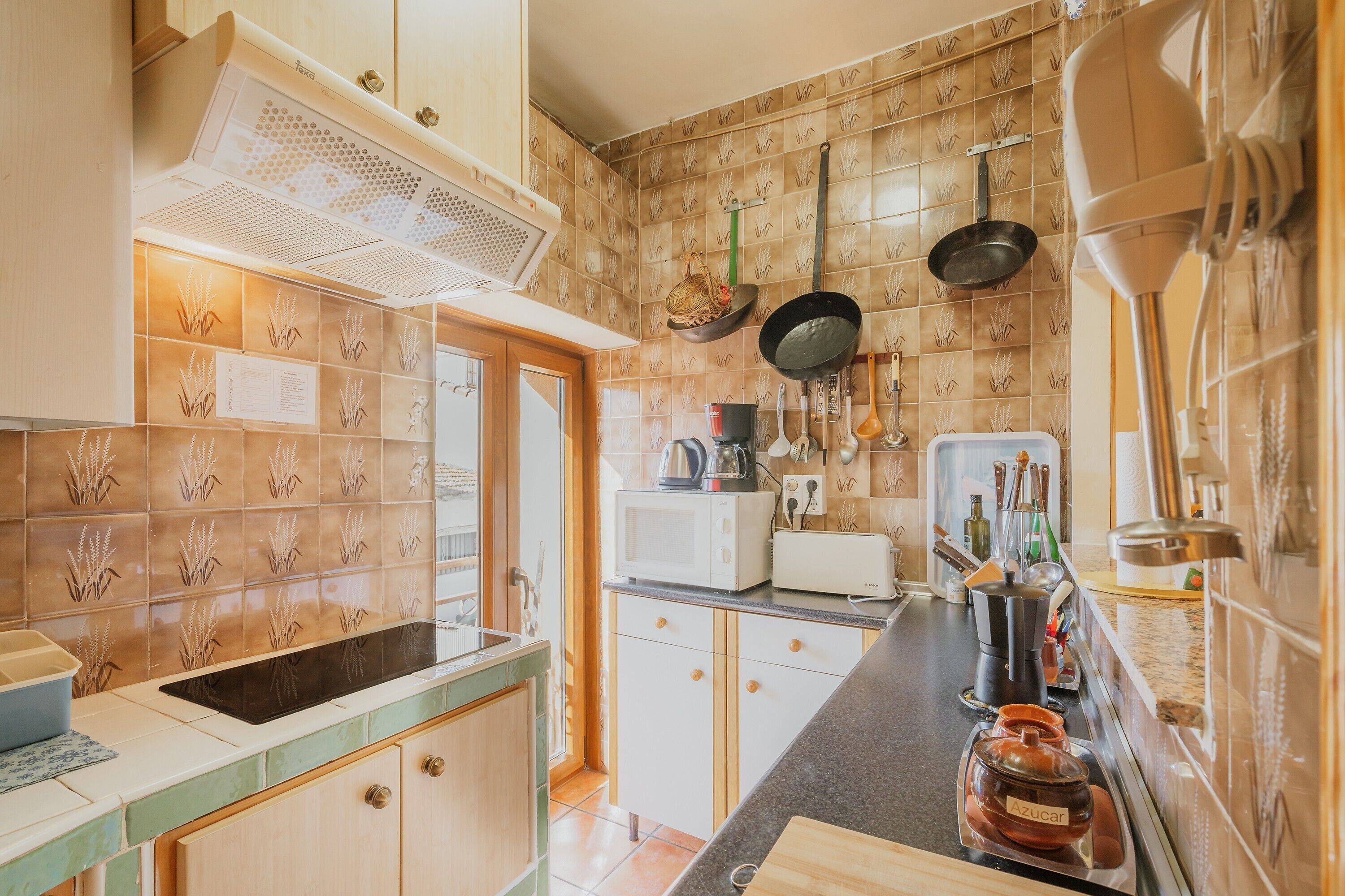 A kitchen with a microwave, stove, and hanging utensils.