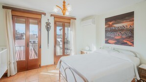 Et soveværelse med en seng, et natbord, en væglampe, en dør med udsigt til en balkon og et billede på væggen.