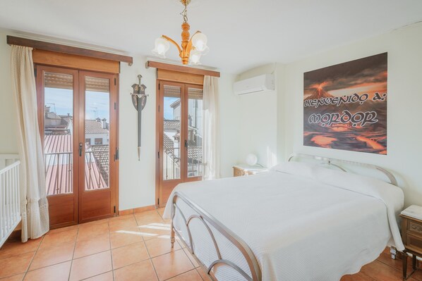 A bedroom with a bed, a nightstand, a wall-mounted lamp, a door with a view to a balcony, and a poster on the wall.