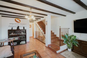 A living room with a wooden staircase, a bookshelf, a television, and a potted plant. - Casa Rivendel: Fantasy-Themed Holiday Home in Sierra de Gredos (Poyales del Hoyo)