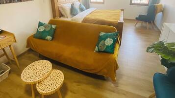 A cozy room with a sofa, two small round tables, a bed with a yellow bedspread, and two windows with curtains.