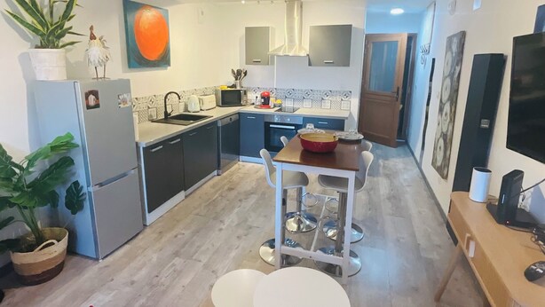 A compact kitchen with modern appliances, a dining area with a small table and chairs, and a red sofa in the foreground. - Mirepoix 4 star apartment (Mirepoix)