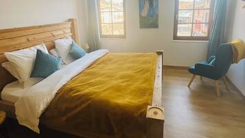 A bedroom with a wooden bed, a chair, and two windows.
