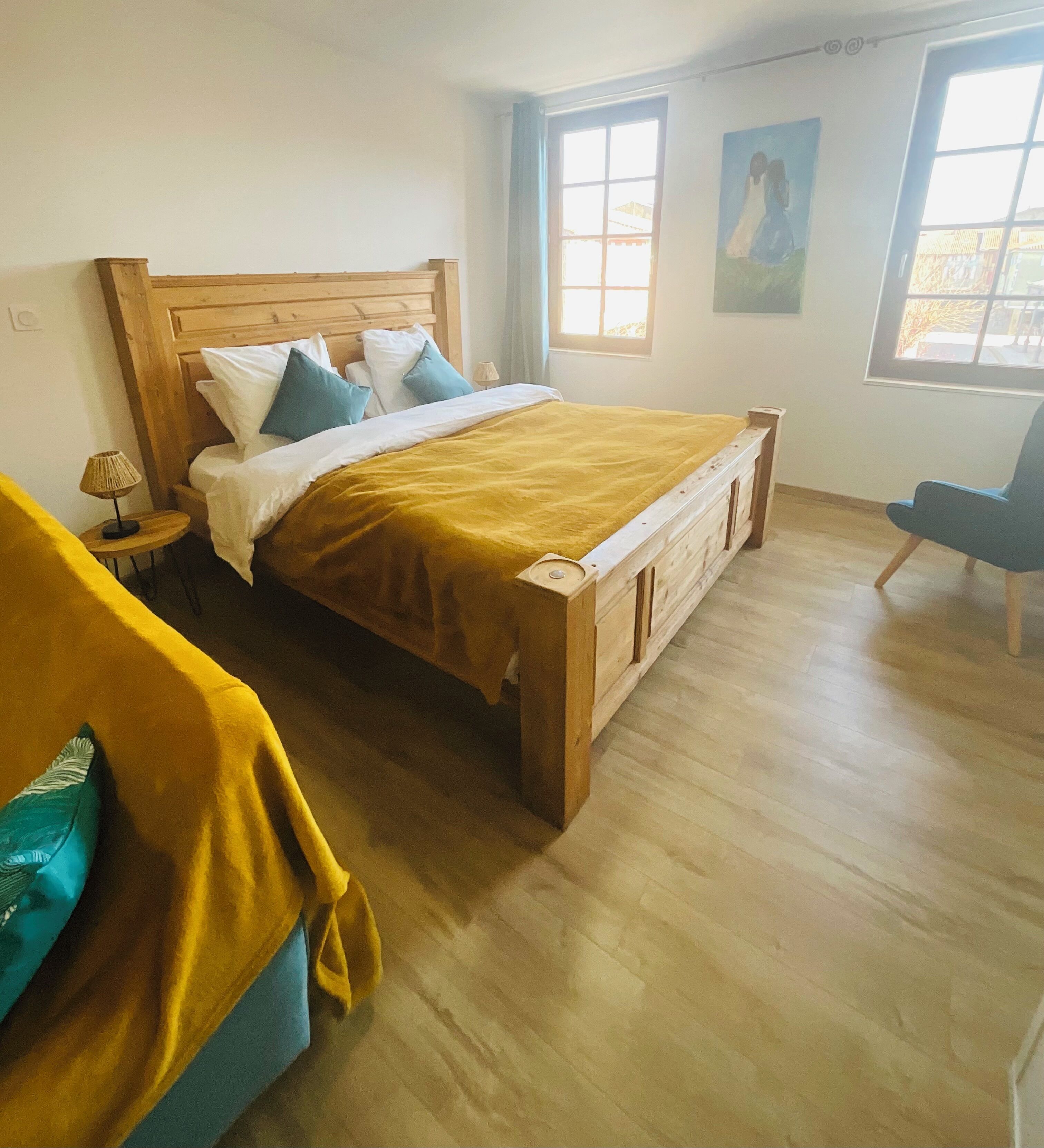 A bedroom with a wooden bed, a small bedside table, a chair, and a window with curtains.