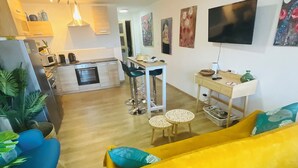 A modern living room with a yellow sofa, a kitchen area with a dining table, and a TV mounted on the wall. - Mirepoix 4 star apartment (Mirepoix)