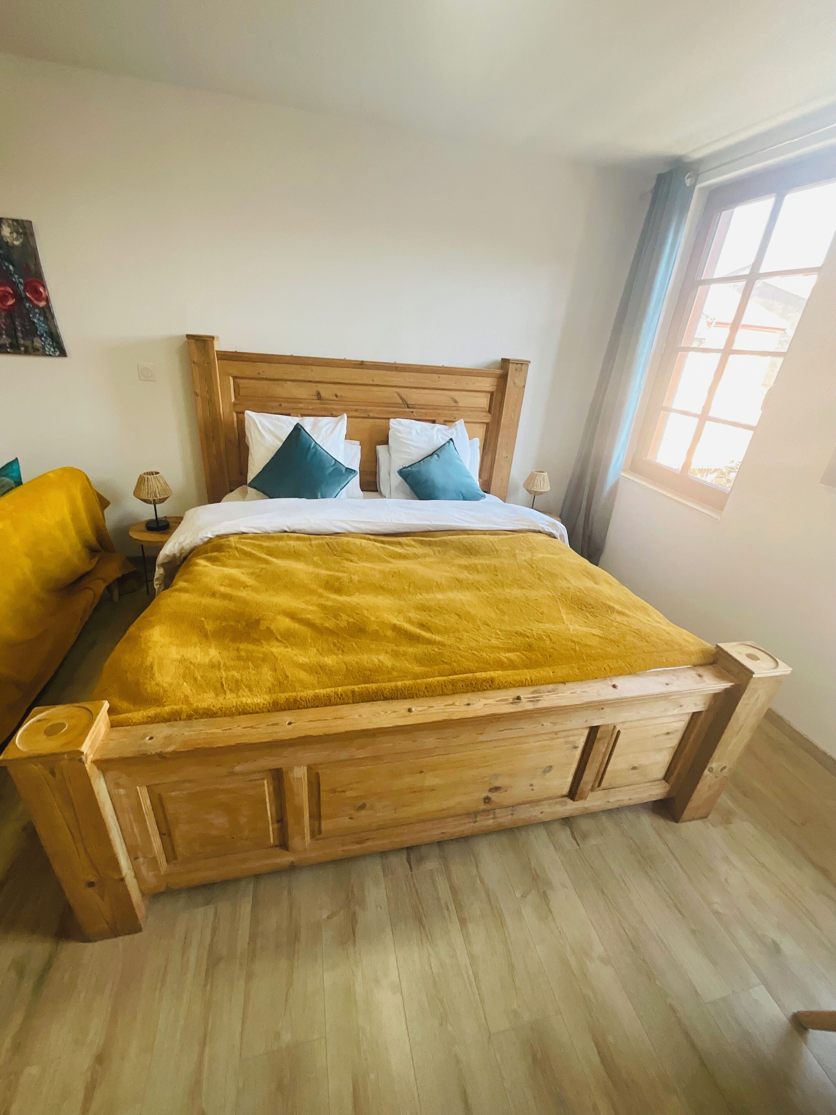 Un lit en bois avec une couverture jaune, deux oreillers et une table de chevet avec une lampe.