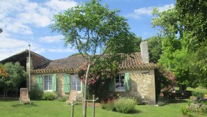 Ein Haus aus Stein mit einem Ziegeldach, einem Rasen und einem Stuhl.