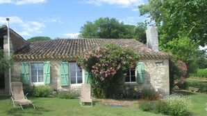 Ein Steinhaus mit Ziegeldach, grünen Fensterläden und einem Garten mit Blumen und Rasen.